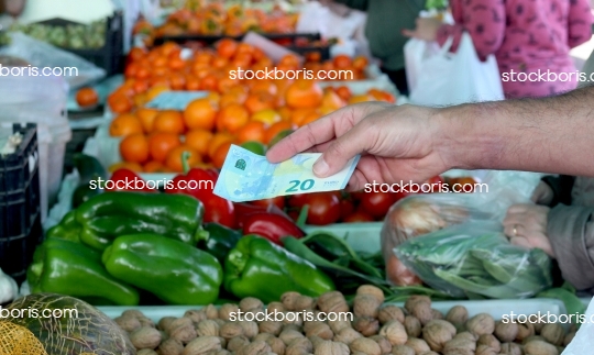 A hand with a 20 euros banknote at a market. Purchasing buying fruits.