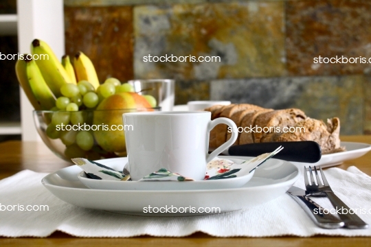 Breakfast table with a coffee mug, bread, knife, bananas, grapes and papaya