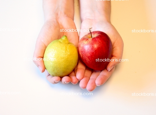 Hands holding a lemon and apple.