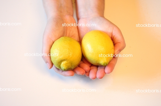 Hands holding two yellow lemons.