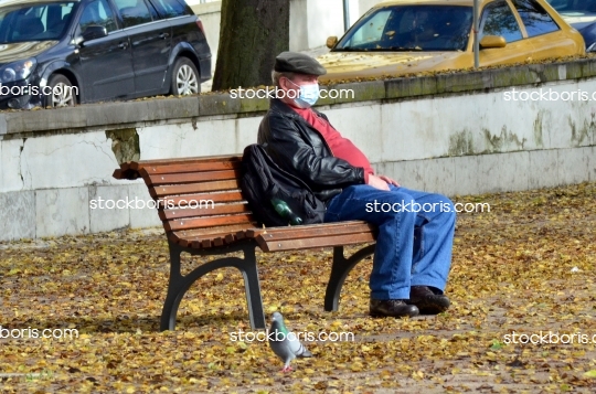 Old calm relaxed senior man sitting waiting on a bench during Coronavirus pandemics.