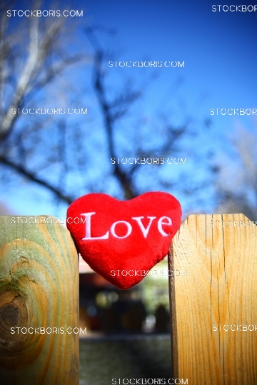 Red love heart plush in a wood fence with a blue sky behind.