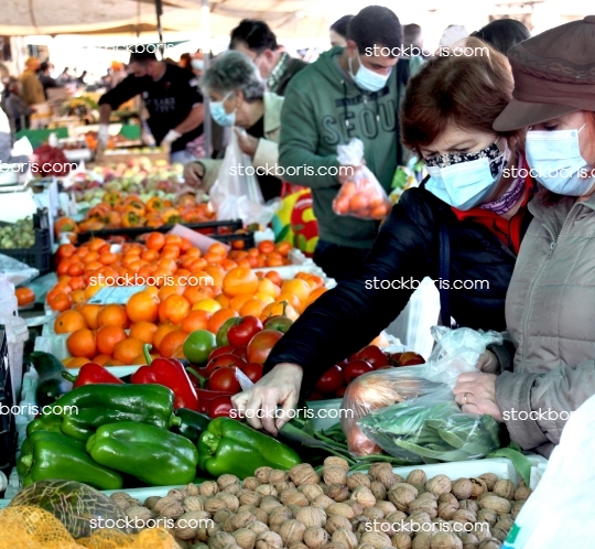 Senior woman with a mask buying vegetables and fruits at a market.